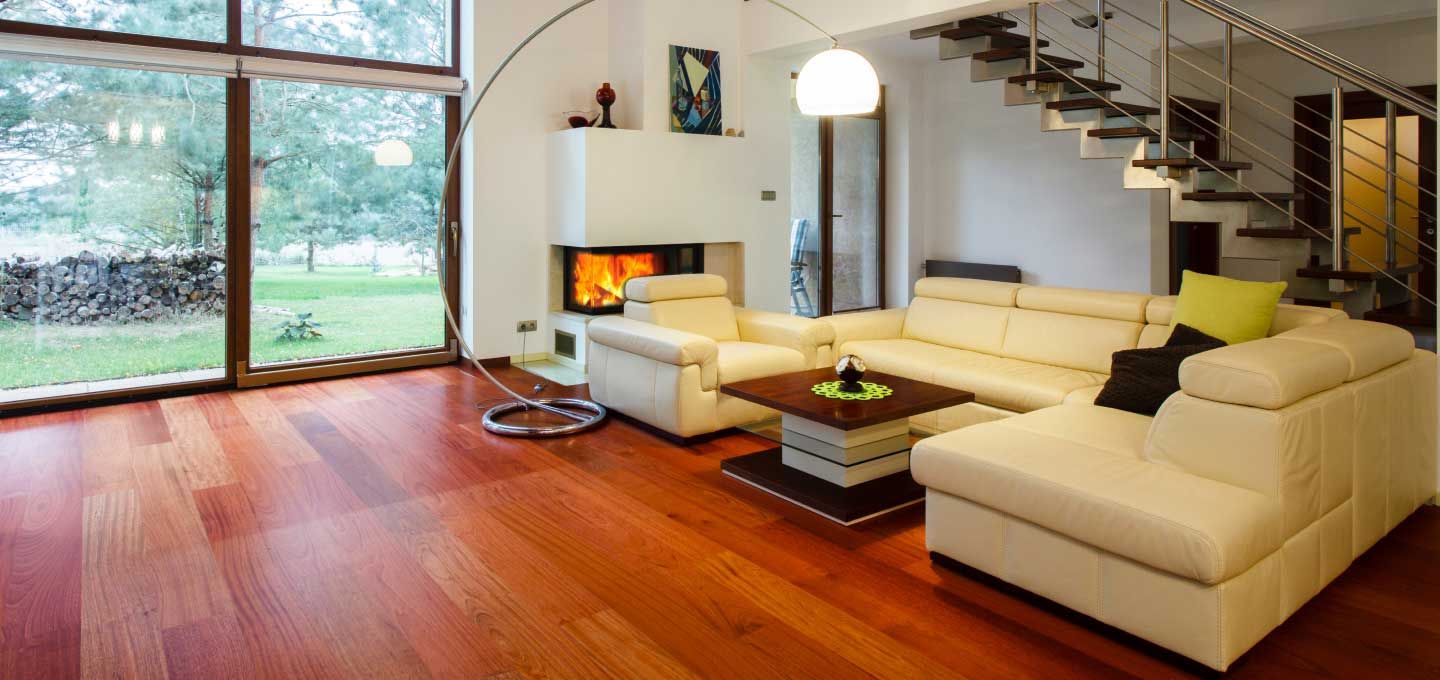 Living room with a warm red hardwood floor under large garden windows